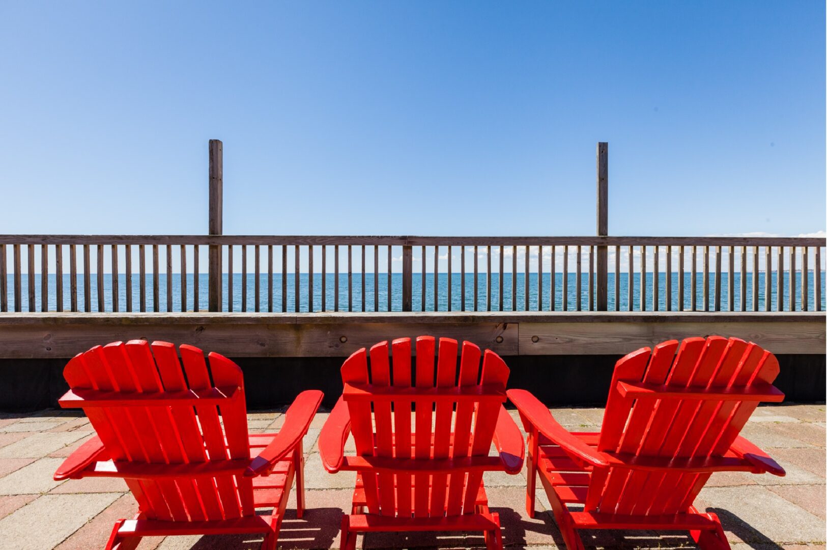 Three red adirondack chairs in front of the ocean.